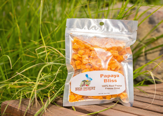 Packaged papaya bites labeled 'Papaya Bliss' by High Desert on a wooden surface with grass in the background.
