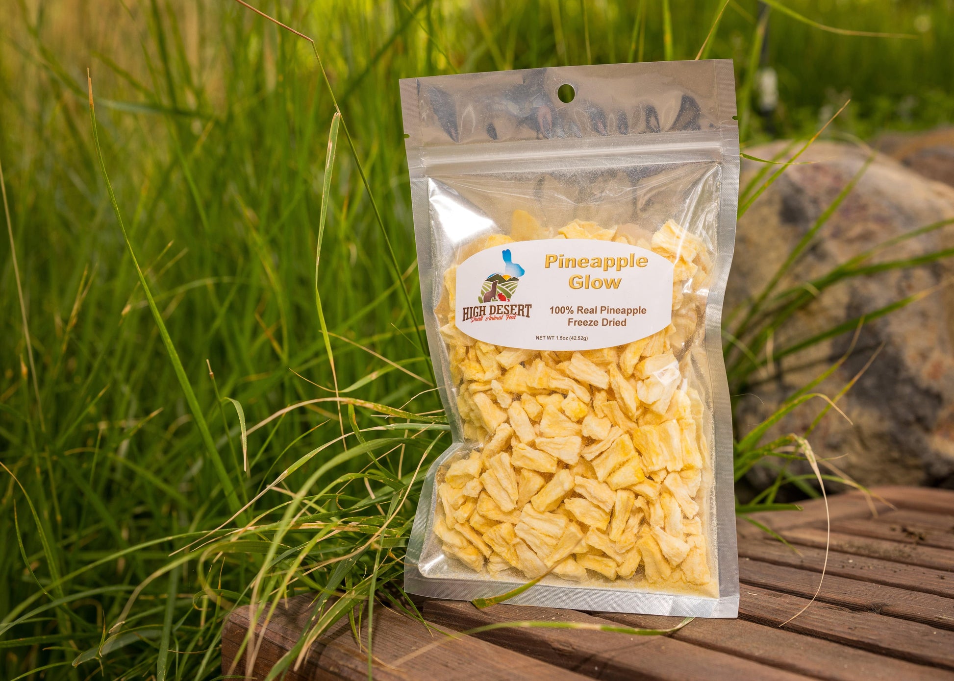 Package of pineapple slices on a wooden surface with grass in the background